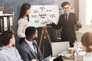 cheerful-coach-explaining-importance-business-plan-young-team-motivational-training-using-board-with-graph_116547-5702